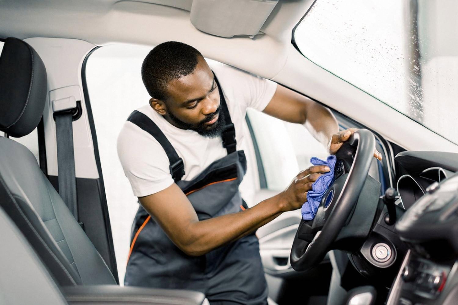 Detailer wiping car interior surfaces with a microfibre cloth while cleaning the cabin
